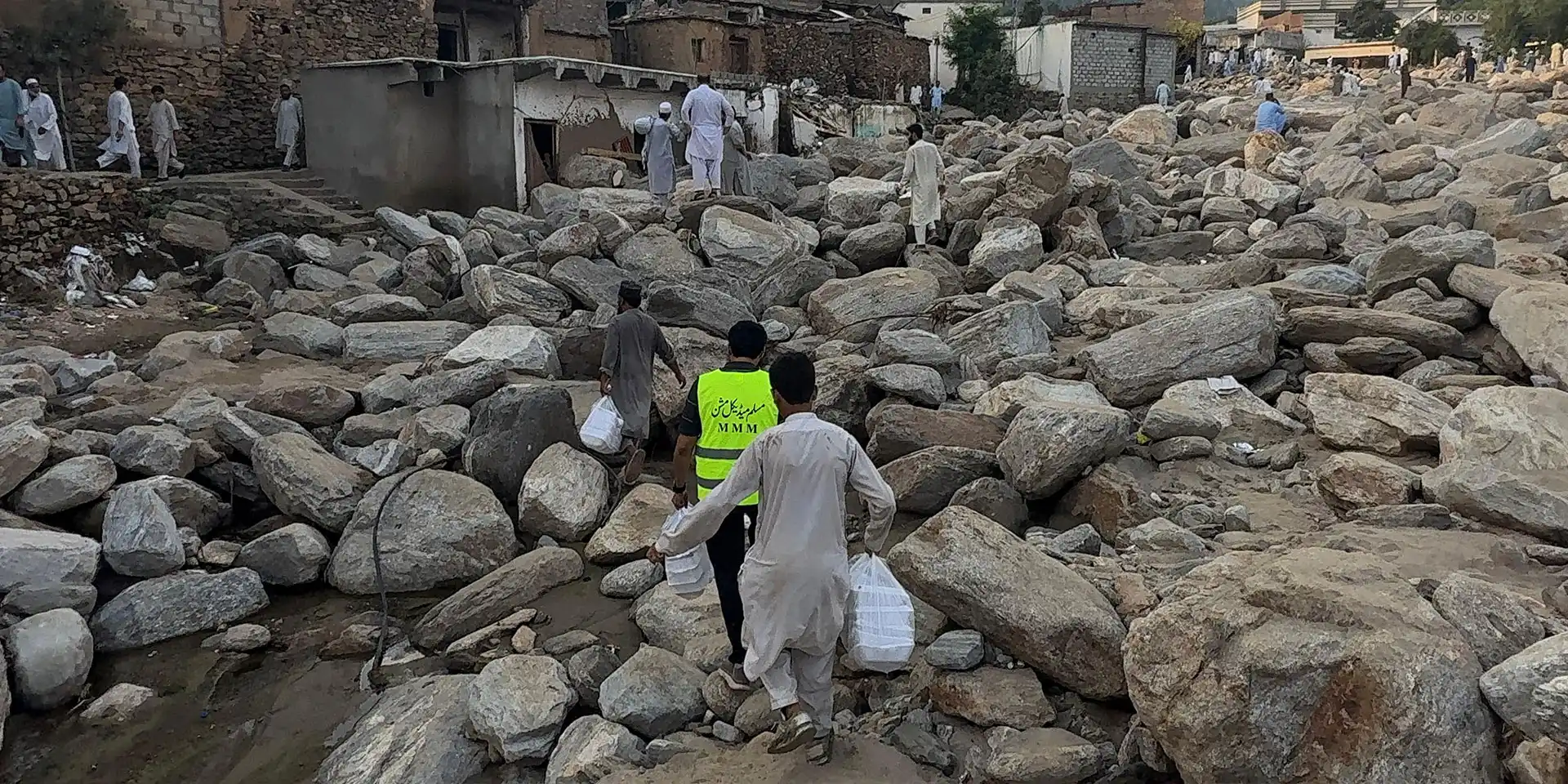 Muslim Medical Mission volunteers carrying relief supplies over boulders through a flood-damaged mountain village